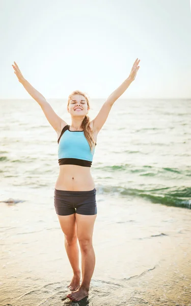 Fitness sport model smiling happy doing exercises during outdoor work out on sunrise. Beautiful caucasian female training outside on seaside in the morning