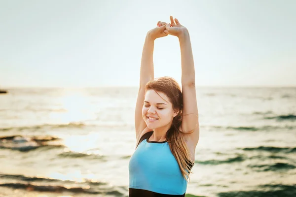 Modello di sport fitness sorridente felice facendo esercizi durante il lavoro all'aperto all'alba. Bella formazione femminile caucasica al di fuori sul mare al mattino — Foto Stock