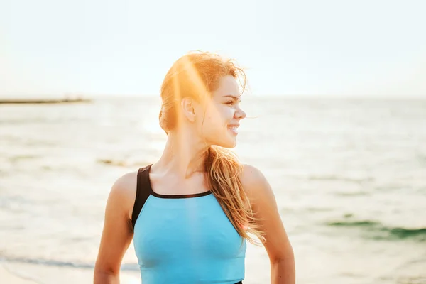 Fitness modelo deportivo sonriendo feliz haciendo ejercicios durante el ejercicio al aire libre a la salida del sol. Hermosa mujer caucásica entrenamiento al aire libre en la playa por la mañana — Foto de Stock