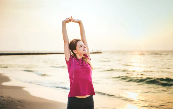 Modello di sport fitness sorridente felice facendo esercizi durante il lavoro all'aperto all'alba. Bella formazione femminile caucasica al di fuori sul mare al mattino — Foto Stock