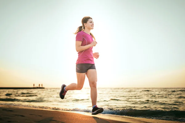 Systemem kobieta. Kobiece kobieta lekkoatletka joggingu podczas słońca na plaży. — Zdjęcie stockowe