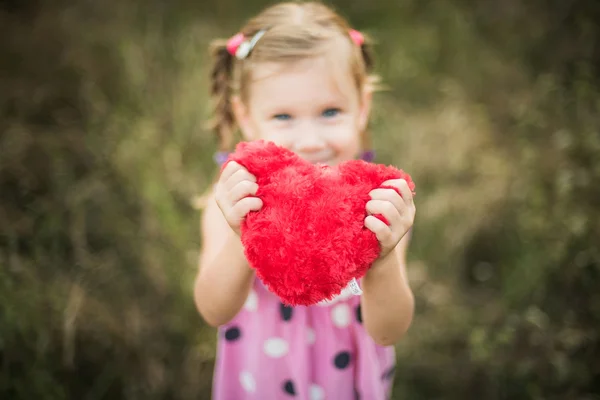 Pequeña chica bonita sosteniendo rojo corazón juguete al aire libre — Foto de Stock