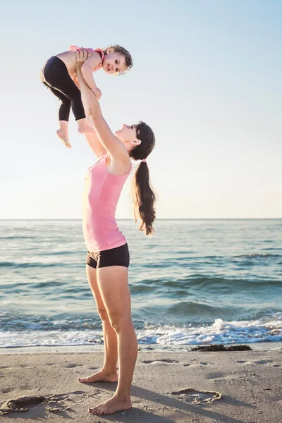 Семейные тренировки - мама и дочь делают упражнения на пляже . — стоковое фото