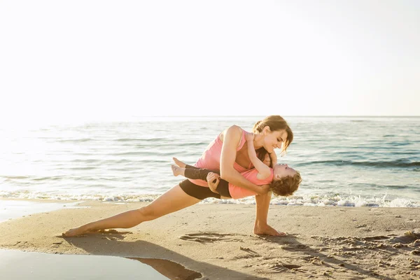 family workout - mother and daughter doing exercises on beach.