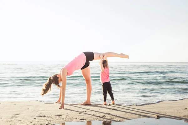 Rodinné cvičení - matka a dcera dělá cvičení na pláži. — Stock fotografie