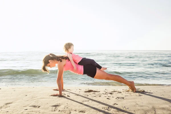 Family workout - mother and daughter doing exercises on beach. — Stock Photo, Image