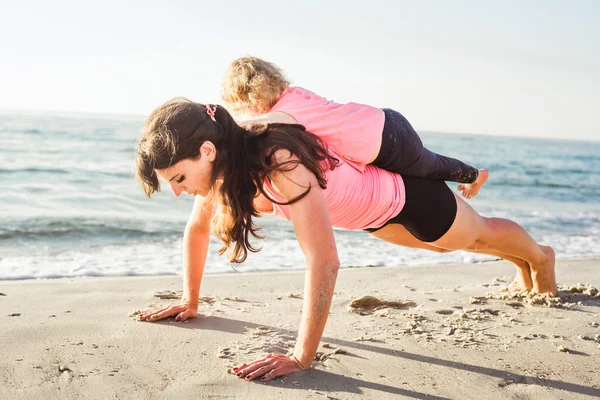 Family workout - mother and daughter doing exercises on beach. — Stock Photo, Image