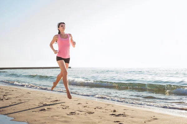 Systemem kobieta. Kobiece kobieta lekkoatletka joggingu podczas słońca na plaży — Zdjęcie stockowe