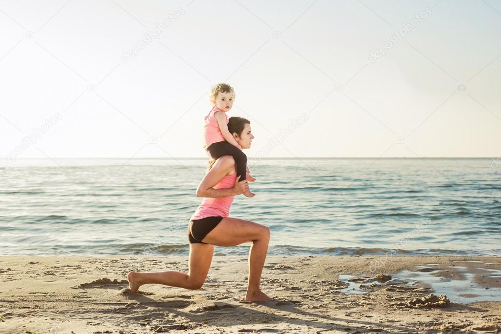 family workout - mother and daughter doing exercises on beach.