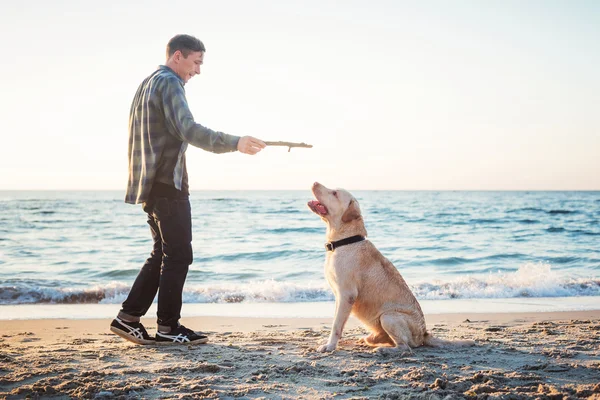 Jeune caucasien mâle jouer avec labrador sur la plage pendant sunri — Photo