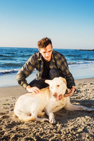 Jeune caucasien mâle jouer avec labrador sur la plage pendant sunri — Photo