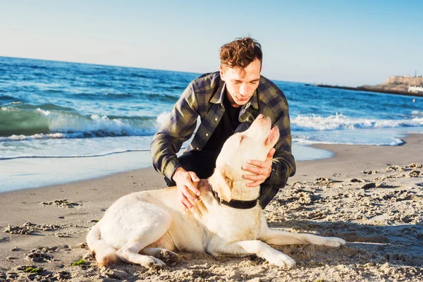 Unga kaukasiska manlig leker med labrador på stranden under sunri — Stockfoto