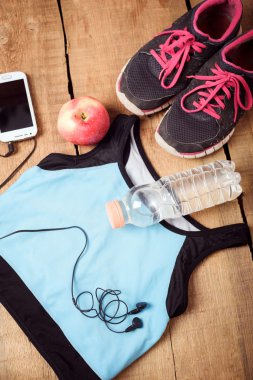 Spor donatımı. Spor ayakkabı, su, elma, mavi üst, akıllı telefon ve kulaklık ahşap arka plan üzerinde. Çalışan için giyim