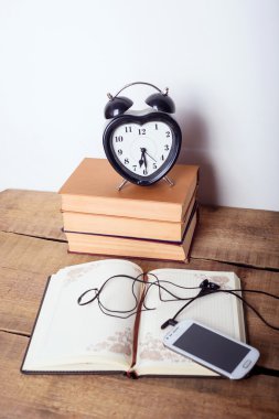 Kitaplar, çalar saat, not defteri, ahşap arka plan üzerinde kulaklık ile cep telefonu. Eğitim donanımları, eğitim kavramı