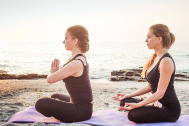 iki genç beyaz kadın gündoğumu sırasında pratik Yoga sahilde