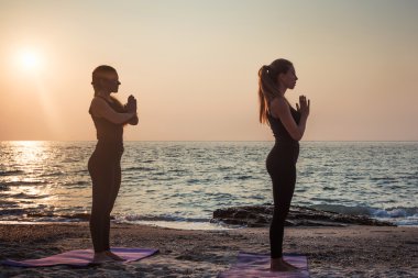 iki genç beyaz kadın gündoğumu sırasında pratik Yoga sahilde