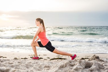 Fitness spor modeli gündoğumu üzerinde açık çalışması sırasında egzersizleri yapıyor. Güzel beyaz kadın eğitim dışında sahil sabah