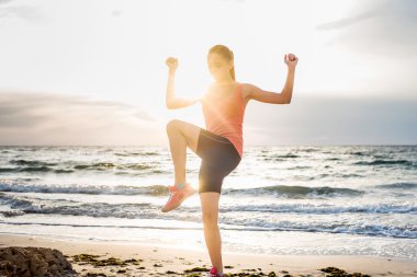 Fitness spor modeli gündoğumu üzerinde açık çalışması sırasında egzersizleri yapıyor. Güzel beyaz kadın eğitim dışında sahil sabah