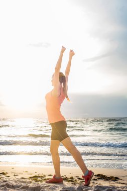 Fitness spor modeli gündoğumu üzerinde açık çalışması sırasında egzersizleri yapıyor. Güzel beyaz kadın eğitim dışında sahil sabah