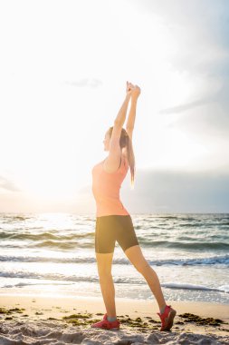 Fitness spor modeli gündoğumu üzerinde açık çalışması sırasında egzersizleri yapıyor. Güzel beyaz kadın eğitim dışında sahil sabah