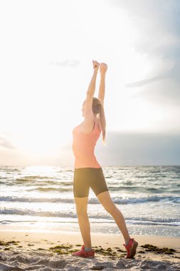 Fitness spor modeli gündoğumu üzerinde açık çalışması sırasında egzersizleri yapıyor. Güzel beyaz kadın eğitim dışında sahil sabah