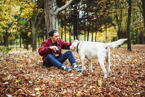 Człowiek pije kawę w parku i grając z labrador pies — Zdjęcie stockowe