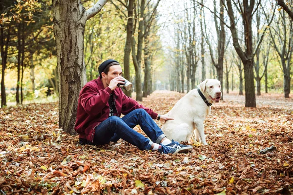 Мужчина пьет кофе в парке и играет с собакой-лабрадором — стоковое фото