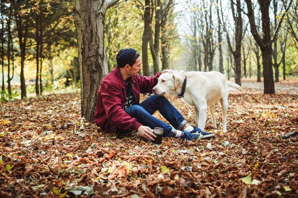 Мужчина пьет кофе в парке и играет с собакой-лабрадором — стоковое фото