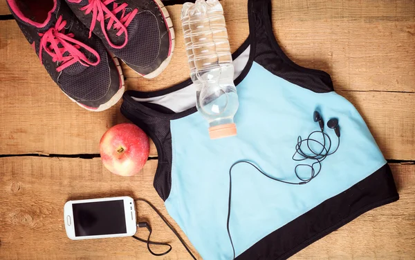 Sportutrustning. Sneakers, vatten, äpple, blå topp, smartphone och hörlurar på trä bakgrund. Kläder för löpning — Stockfoto