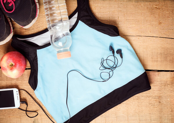 Sport equipment. Sneakers, water, apple, blue top, smartphone and earphones on wooden background. Clothes for running