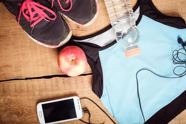 Sportutrustning. Sneakers, vatten, äpple, blå topp, smartphone och hörlurar på trä bakgrund. Kläder för löpning — Stockfoto