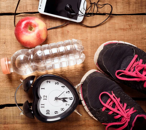 Attrezzature sportive. Sneakers, acqua, mela, sveglia, smartphone e auricolari su sfondo legno. Vestiti per correre. Mattina in esecuzione concetto — Foto Stock