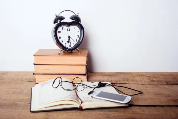 books, alarm clock, notepad, cellphone with earphones  on wooden background. Education equipment, education concept