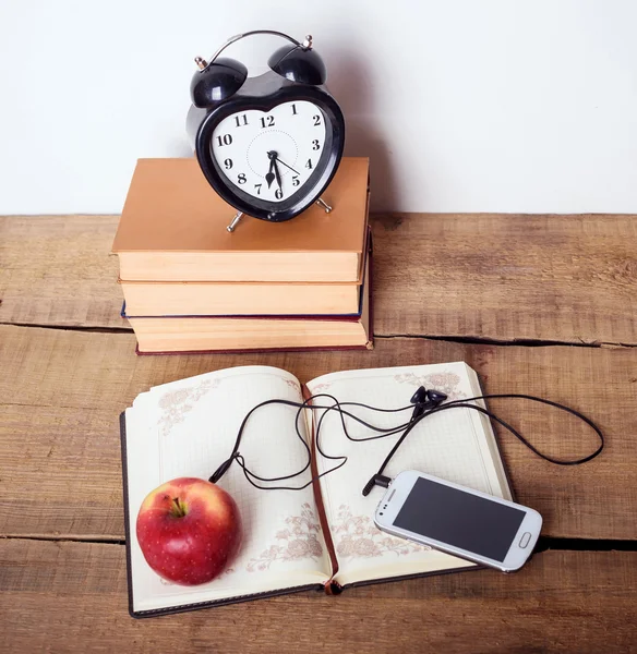 books, alarm clock, notepad, cellphone with earphones and apple on wooden background. Education equipment, education concept