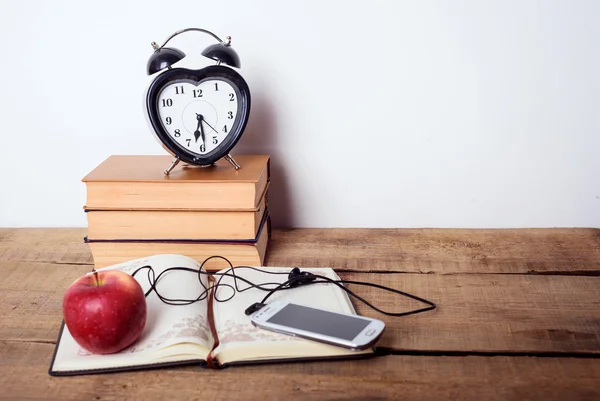 books, alarm clock, notepad, cellphone with earphones and apple on wooden background. Education equipment, education concept