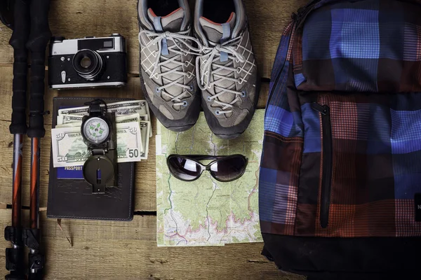 travel equipment - hiking boots, map, backpack, trekking poles, vintage camera, sunglasses, compass, cellphone, earphones, notebook, pen, apple, passport and money