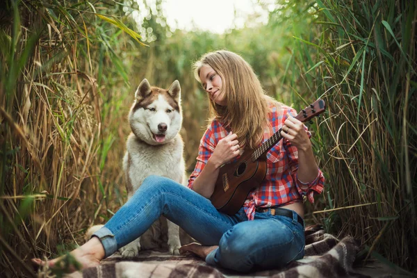 Junge kaukasische Frau spielt Ukulele. Hündin mit sibirischem Husky-Hund spielt im Freien Gitarre — Stockfoto