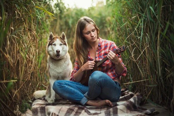 Νεαρή γυναίκα καυκάσιος παίζοντας γιουκαλίλι. Θηλυκό με Σιβηρικό γεροδεμένο σκυλί που παίζει κιθάρα σε εξωτερικούς χώρους — Φωτογραφία Αρχείου