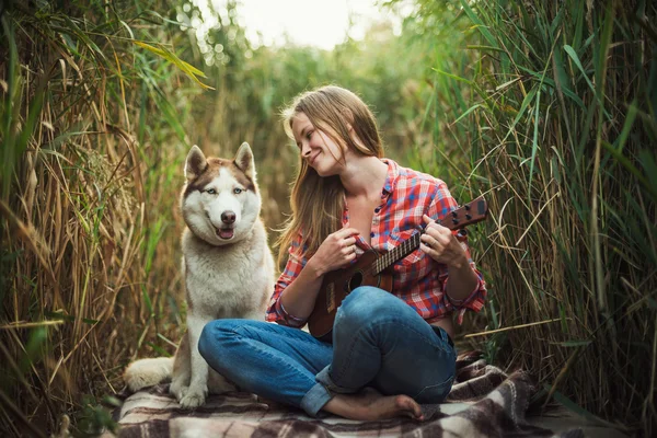 Junge kaukasische Frau spielt Ukulele. Hündin mit sibirischem Husky-Hund spielt im Freien Gitarre — Stockfoto