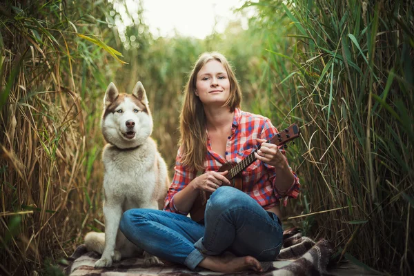 Junge kaukasische Frau spielt Ukulele. Hündin mit sibirischem Husky-Hund spielt im Freien Gitarre — Stockfoto