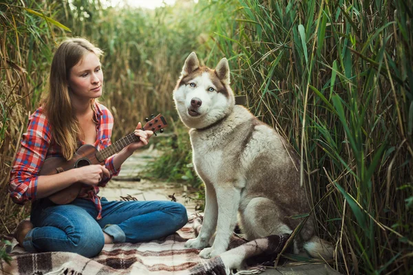 Νεαρή γυναίκα καυκάσιος παίζοντας γιουκαλίλι. Θηλυκό με Σιβηρικό γεροδεμένο σκυλί που παίζει κιθάρα σε εξωτερικούς χώρους — Φωτογραφία Αρχείου