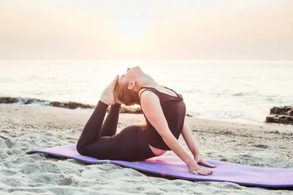 Giovane femmina caucasica che pratica yoga sulla spiaggia durante l'alba — Foto Stock