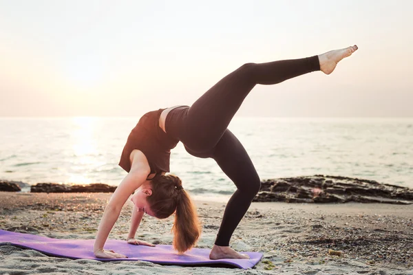 Junge kaukasische Frau praktiziert Yoga am Strand bei Sonnenaufgang — Stockfoto