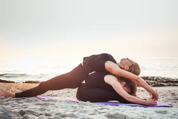 Zwei junge kaukasische Frauen praktizieren Yoga am Strand bei Sonnenaufgang — Stockfoto