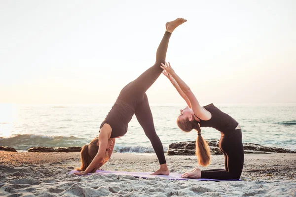 Zwei junge kaukasische Frauen praktizieren Yoga am Strand bei Sonnenaufgang — Stockfoto