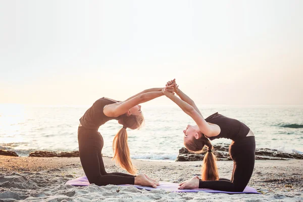 Zwei junge kaukasische Frauen praktizieren Yoga am Strand bei Sonnenaufgang — Stockfoto