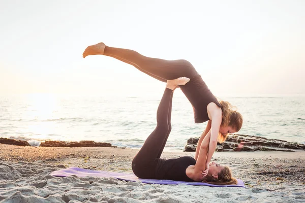 Zwei junge kaukasische Frauen praktizieren Yoga am Strand bei Sonnenaufgang — Stockfoto