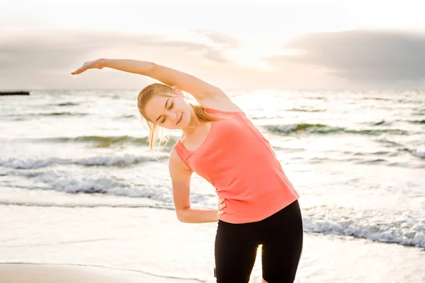 Fitness sport model  doing exercises during outdoor work out on sunrise. Beautiful caucasian female training outside on seaside in the morning