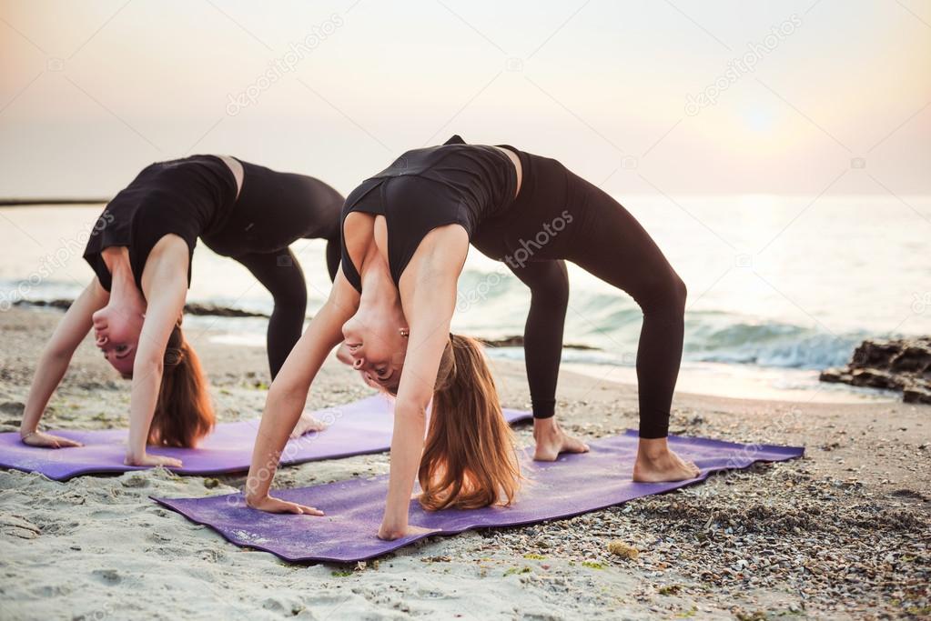 two young caucasian females practicing yoga on beach during sunrise