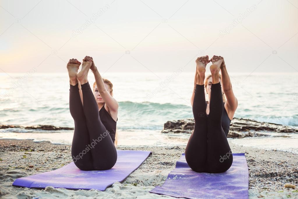 two young women practicing yoga on beach